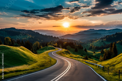 A winding road going into the distance by the setting sun, mountains on the horizon, green hills and forest on the sides