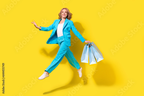 Full size photo of elegant adorable cute girl dressed blue jacket trousers run shopping hold new clothes isolated on yellow background
