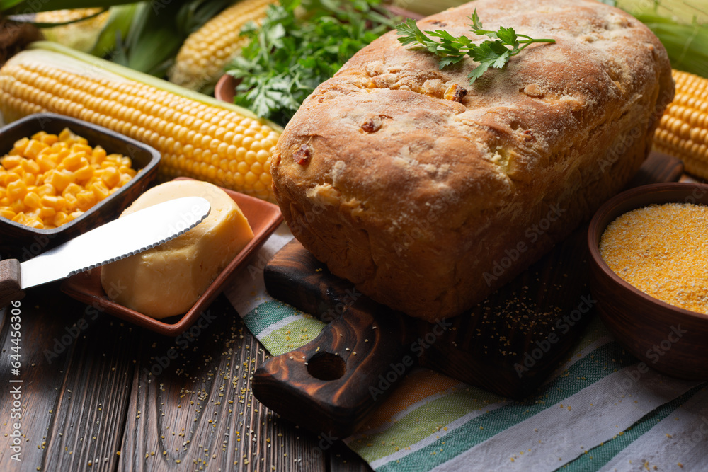 Rustic homemade loaf of cornbread on wooden kitchen table. Cobs and butte aside
