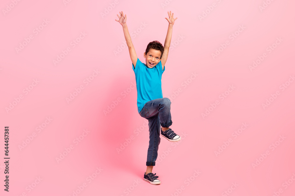 Full length photo of carefree impressed small boy wear blue t-shirt having fun rising hands arms isolated pink color background Full length photo of carefree impressed small boy wear blue t-shirt having fun rising hands arms isolated pink color background