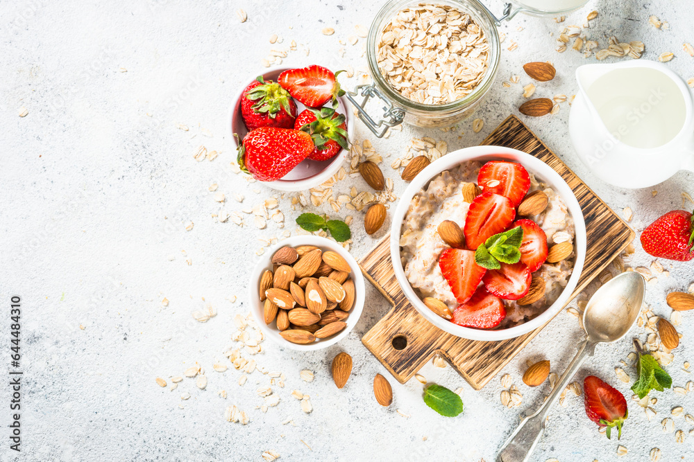 Oatmeal porridge with fresh strawberry and nuts on white background. Healthy breakfast. Top view with copy space.