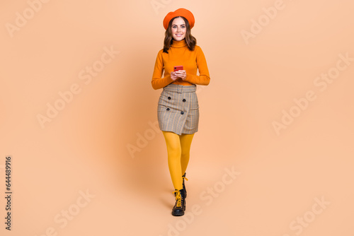 Full length photo of adorable cheerful lady wear trendy outfit walking store center bun modern device isolated on beige color background