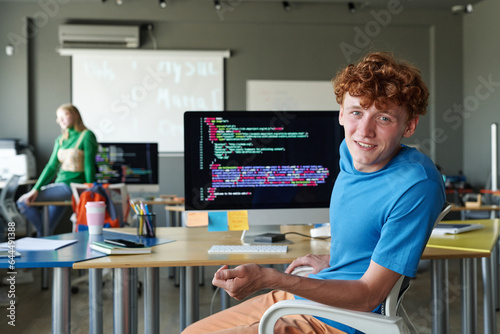 Portrait of schoolboy smiling at camera while working with computer codes on computer in the classroom