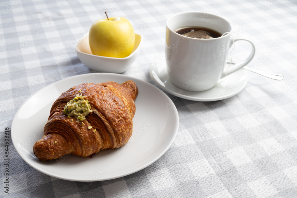 Breakfast, with brioche on a white plate, cup of tea, and an apple. Breakfast, with brioche on a white plate, cup of tea, and an apple.