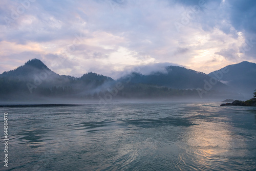 A wide  full-flowing mountain river with a fast current at dawn or sunset. Mountains and forest in the fog. A large turquoise-colored mountain river Katun in the Altai Mountains  Altai Republic.