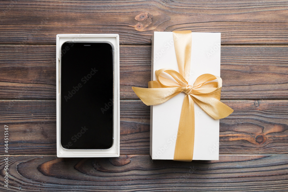 Fototapeta premium Opened gift box with gold ribbon and smartphone on color background, top view. Blank open box packaging mockup , Template for your design - branding mockup