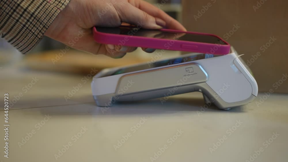 Side view closeup POS terminal with female hand approaching smartphone and leaving. Close-up unrecognizable young Caucasian woman paying in shop cafe with cashless payment using phone app Side view closeup POS terminal with female hand approaching smartphone and leaving. Close-up unrecognizable young Caucasian woman paying in shop cafe with cashless payment using phone app