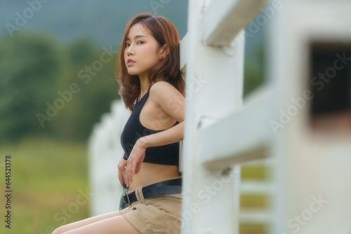 A beautiful Asian woman sitting on a white fence.