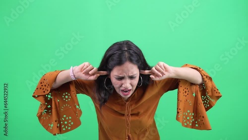 Beautiful Indian Young woman putting fingers on her ears, don't want to listen anything. Woman blocking her ears Shouting No And Shaking Head Posing Standing On chroma green Studio Background.