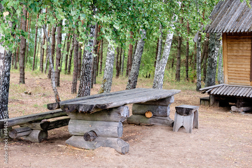 An old table made of tree trunks next to a part of the house in the forest