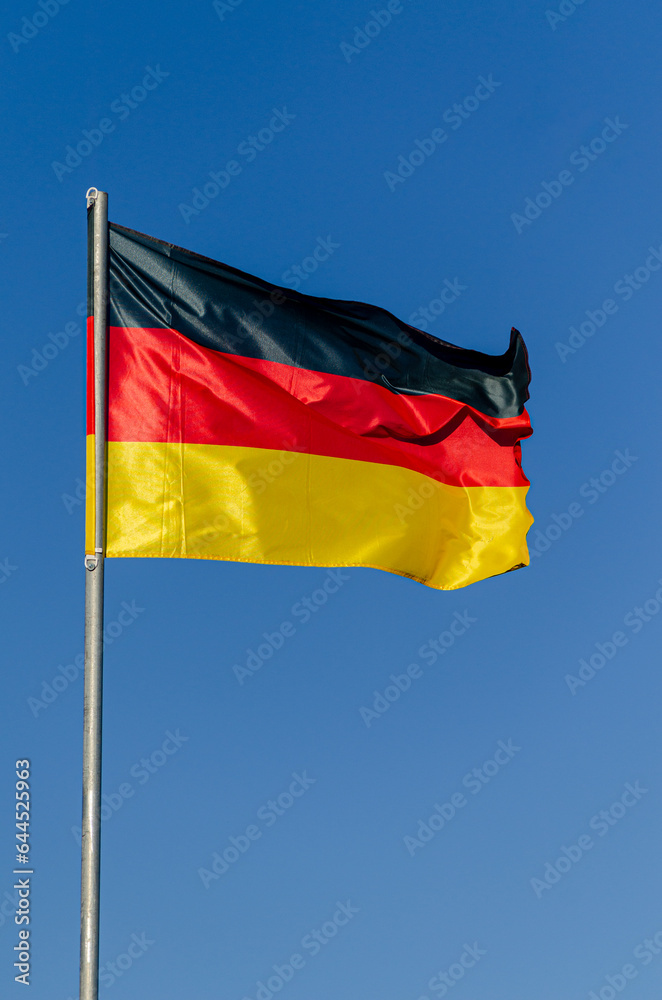 Germany's flag fluttering in the wind on a blue sky day. Germany's flag fluttering in the wind on a blue sky day.