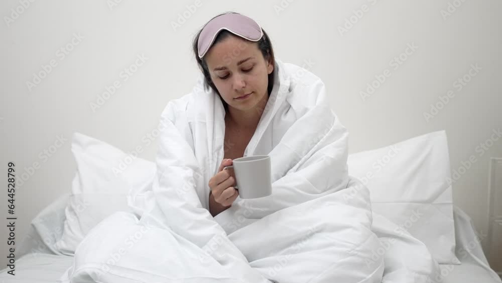 Wrapped in a blanket, sleepy lady sits on bed, coffee in hand, grappling with sleep issues caused by insomnia. Wrapped in a blanket, sleepy lady sits on bed, coffee in hand, grappling with sleep issues caused by insomnia.