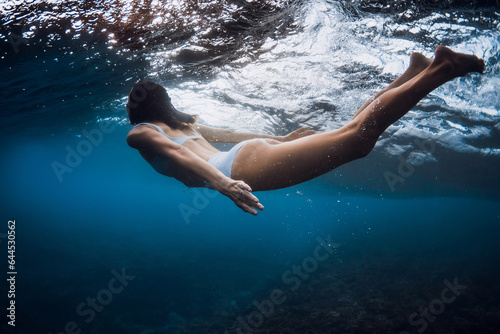 Woman swim and dive under wave in blue ocean.