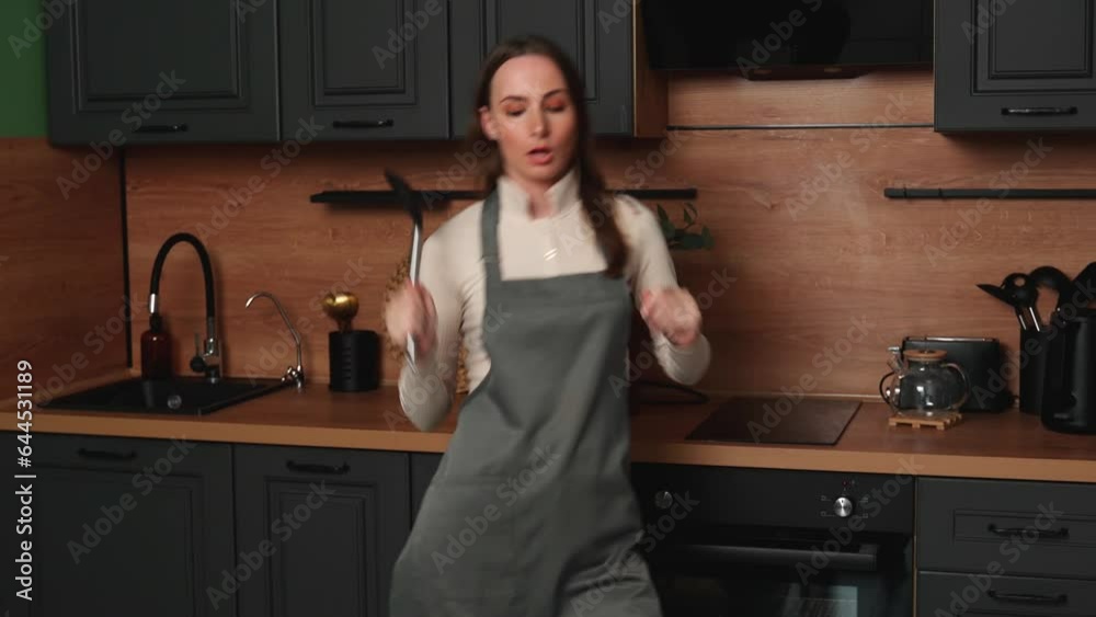 Happy young housewife woman sings and dances while cooking breakfast in the kitchen. 