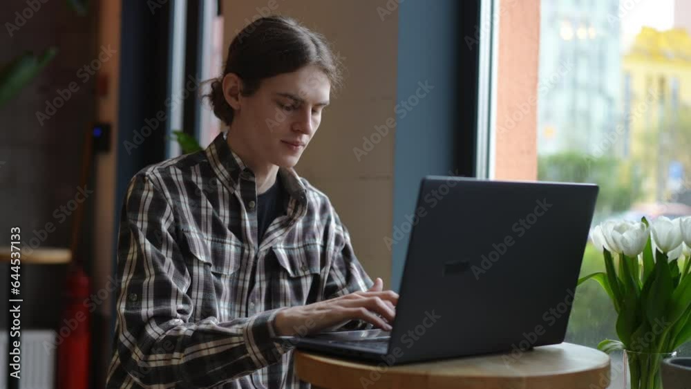 Young man smiling typing on laptop keyboard sitting at table in coffee house. Portrait of male Caucasian freelancer working online indoors in urban city in cafe Young man smiling typing on laptop keyboard sitting at table in coffee house. Portrait of male Caucasian freelancer working online indoors in urban city in cafe