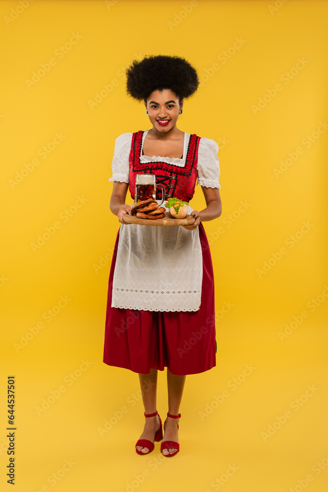 african american oktoberfest waitress holding wooden tray with beer and delicious treat on yellow african american oktoberfest waitress holding wooden tray with beer and delicious treat on yellow