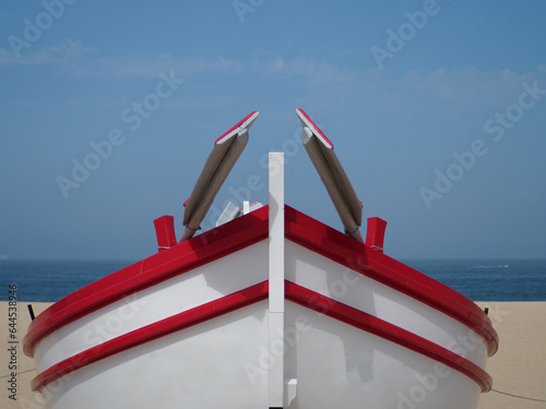 Traditional fishing boat painted red and white on the beach of Nazaré, Portugal.