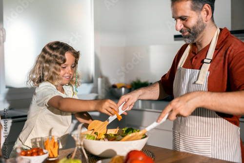 Handsome father cooking healthy salad with his kind daughter in the kitchen at home