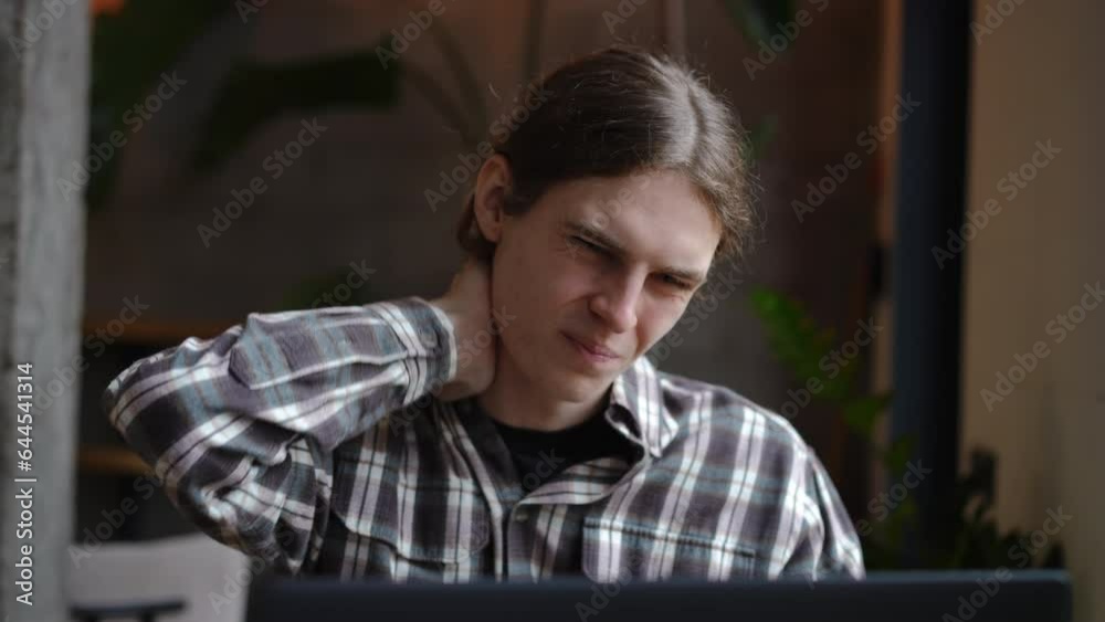 Tired focused young man with painful neck messaging online sitting at table in cafe. Front view portrait of concentrated Caucasian freelancer working online in slow motion in coffee house Tired focused young man with painful neck messaging online sitting at table in cafe. Front view portrait of concentrated Caucasian freelancer working online in slow motion in coffee house