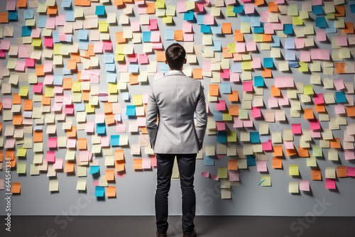 A picture of man standing in front of a wall covered in sticky notes, back view, creative concept of strategic business planning, organization of thinking.  photo
