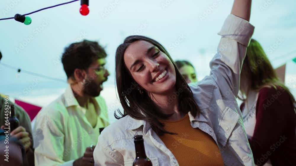Slow motion of a joyful young adult woman smiling and dancing on party weekend celebration with friends. Happy layful female enjoying the music on a festival event. Girl having fun on a dusk fiesta