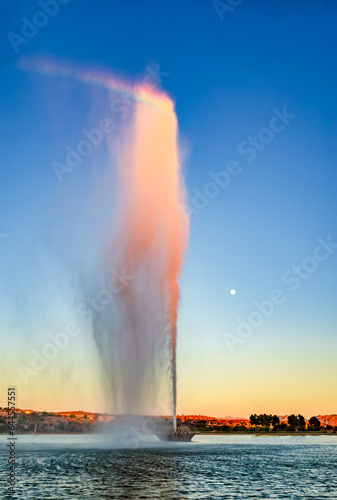 A rainbow forms at the top of the spray from the fountain in Fountain Hills Arizona at dusk with a full moon