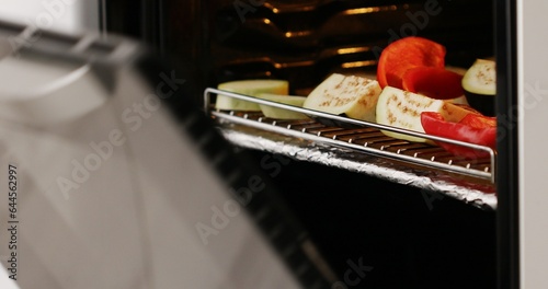 Cooking grilled vegetables. A tray with zucchini, eggplant, red bell peppers and tomatoes is placed in the oven. Food preparation. Close-up.