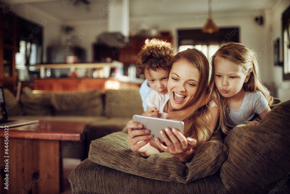 Happy young mother and her children using a smartphone on the couch in the living room at home Happy young mother and her children using a smartphone on the couch in the living room at home