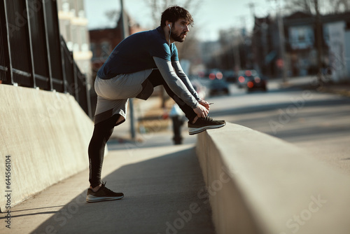 Young man tying his shoelaces while out jogging and exercising in the city photo