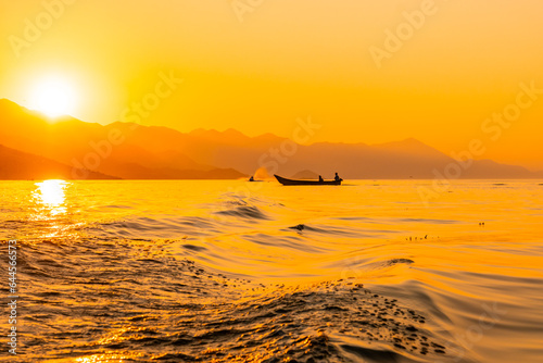 Silhouette of a fishing boat with a fisherman fishing in the orange sunset of Shkoder Lake in Shiroka. Albania photo