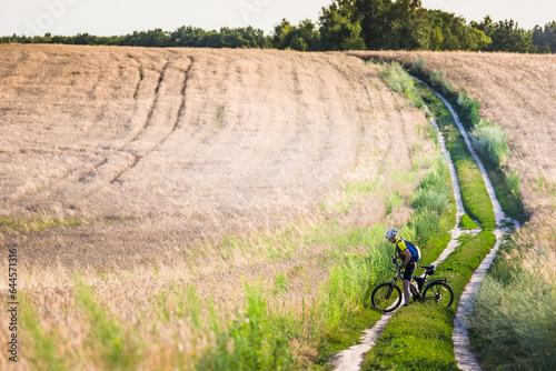 Young man cycling on a rural road through summer meadow