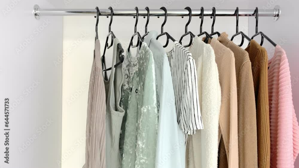 A woman chooses an outfit from a closet with stylish clothes. Women's wardrobe sweatshirts, shirts and blouses in neutral light colors. Concept: organization of the perfect order in the wardrobe