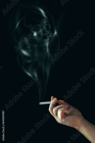 The human hand is holding a cigarette. Smoke in the shape of a skull.
