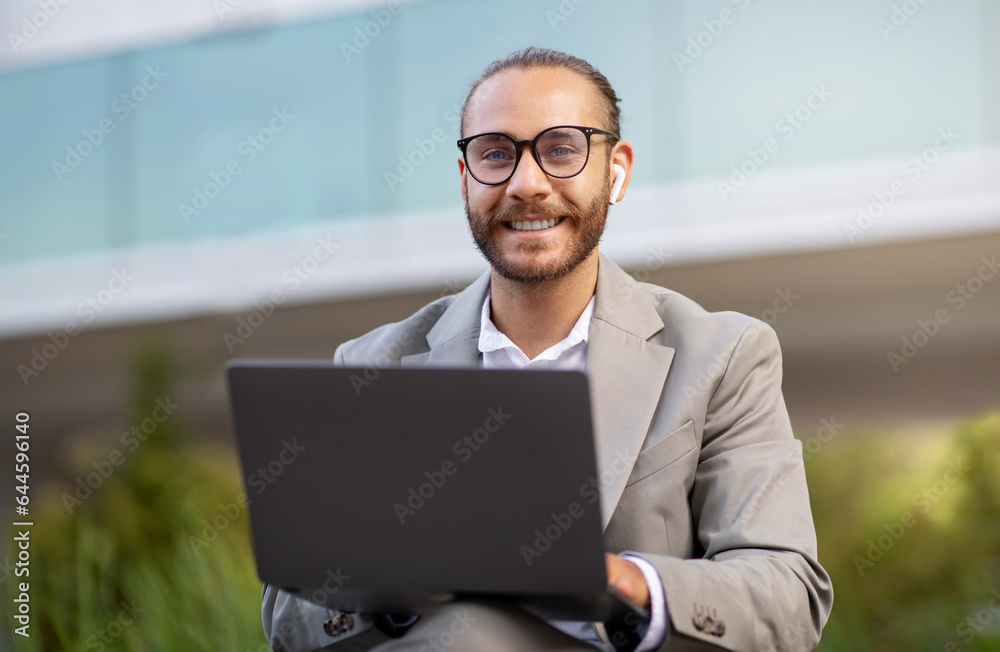 Portrait Of Handsome Young Businessman In Suit Working On Laptop Outdoors