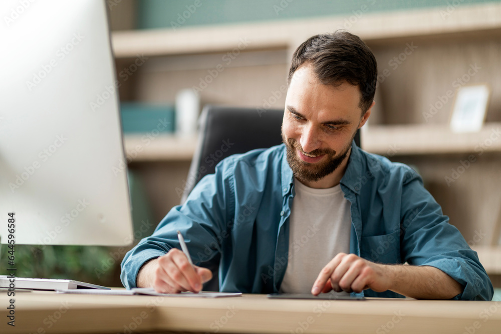 Smiling Businessman Using Digital Tablet And Taking Notes To Notebook In Office Smiling Businessman Using Digital Tablet And Taking Notes To Notebook In Office