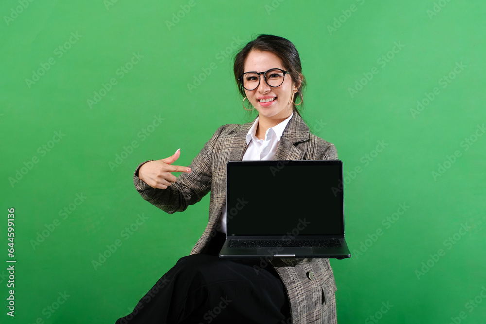 Smiling Asian business woman showing laptop screen with hands pointing at blank laptop screen isolated on green background Smiling Asian business woman showing laptop screen with hands pointing at blank laptop screen isolated on green background