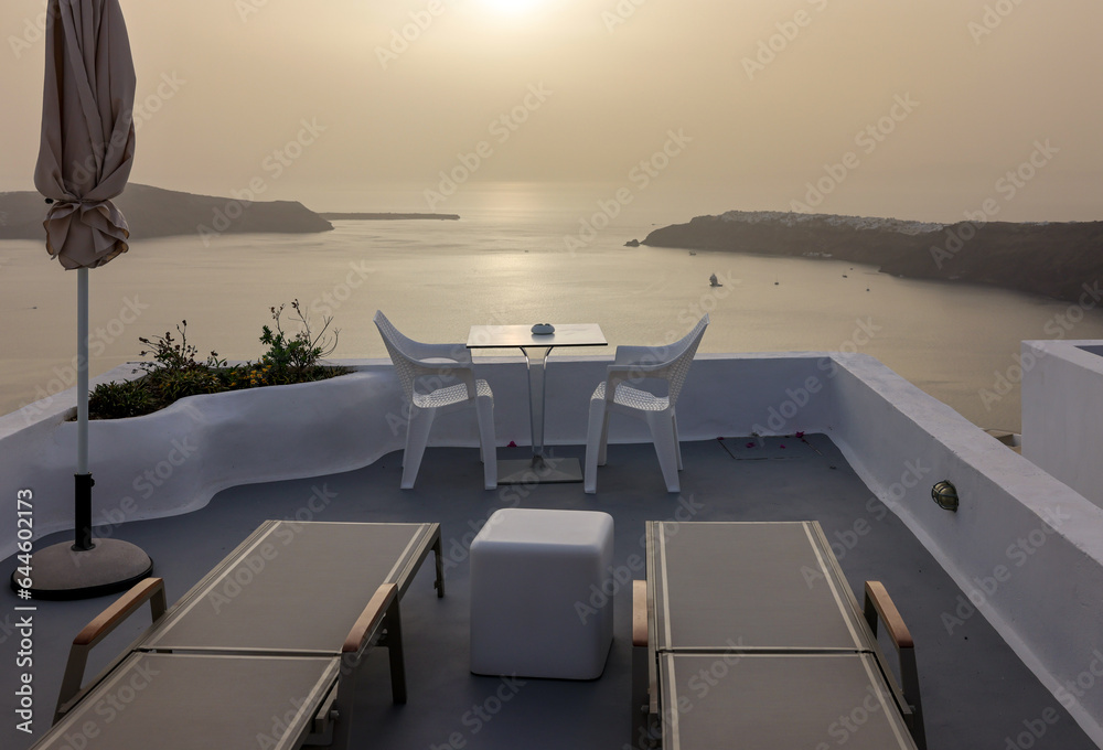 Sun loungers and chairs on terrace in the village of Imerovigli with amazing view of sunset over caldera in Santorini, Greece