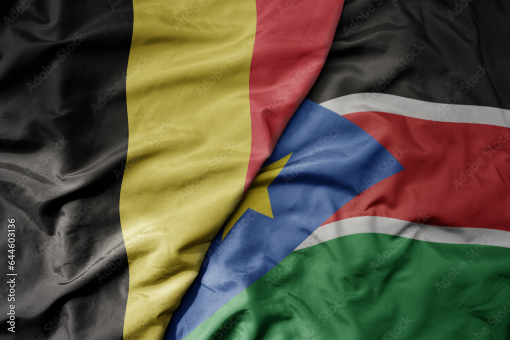big waving national colorful flag of belgium and national flag of south sudan .
