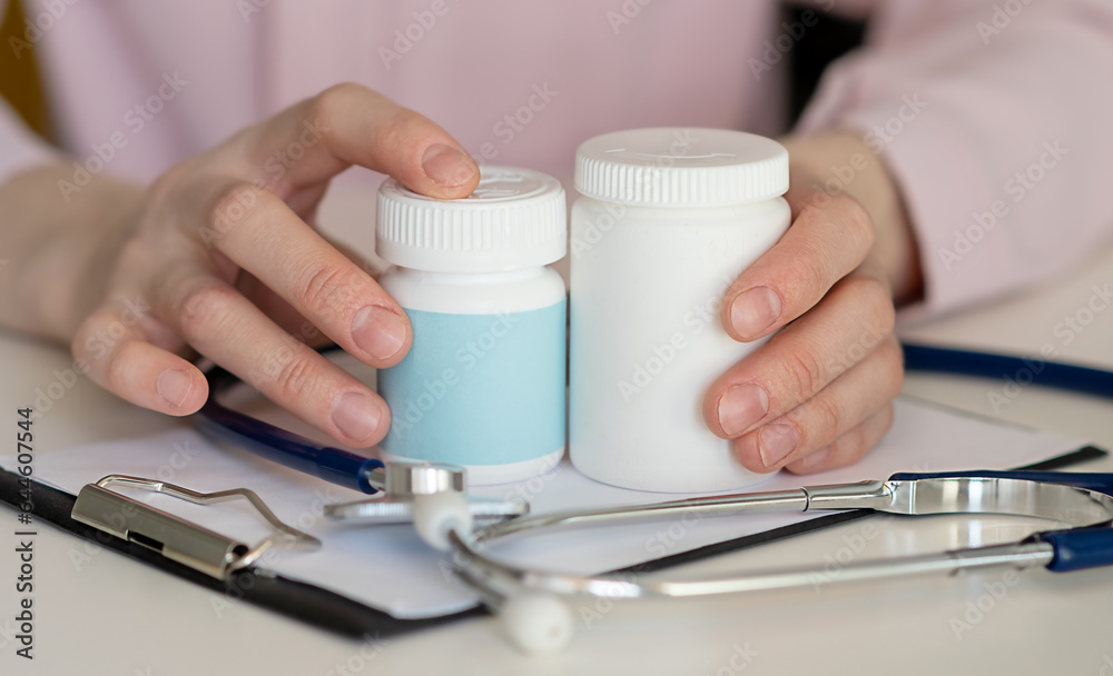 Doctor in white coat write prescription at clinic. Close-up of jar of pills in femail hand. Folder with forms and tonometer are on table.