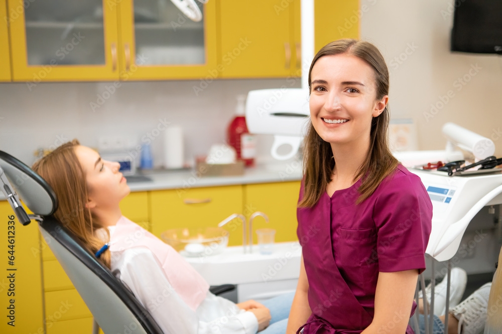Female dentist looks at the camera while patient waiting for the procedure sitting on the medical chair Female dentist looks at the camera while patient waiting for the procedure sitting on the medical chair