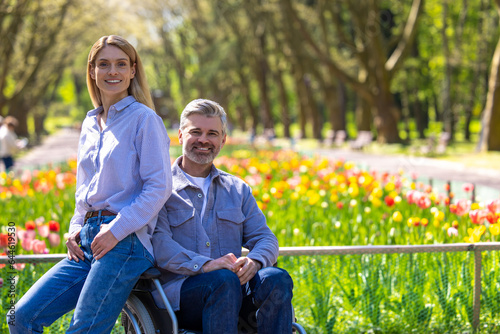 Woman and disabled man in wheelchair walking in park, romantic walking. © zinkevych