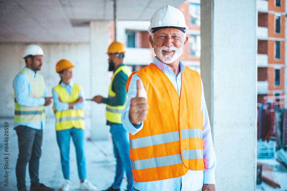 An engineer giving OK sign at construction site. Portrait of happy architect with clipboard gesturing thumbs up outside building. Smiling architect in a construction site An engineer giving OK sign at construction site. Portrait of happy architect with clipboard gesturing thumbs up outside building. Smiling architect in a construction site
