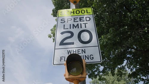 Handheld slow motion view of a school 20 miles per hour when flashing mph speed limit sign near educational building in suburb photo