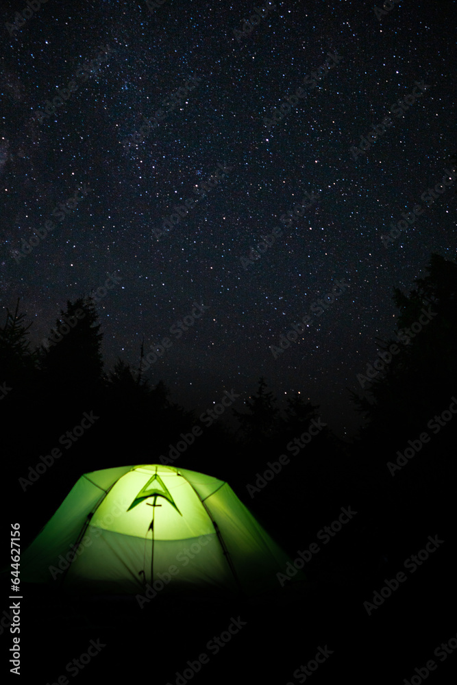 Night sky with bright stars and green tent on the top of the mountain. Camping.