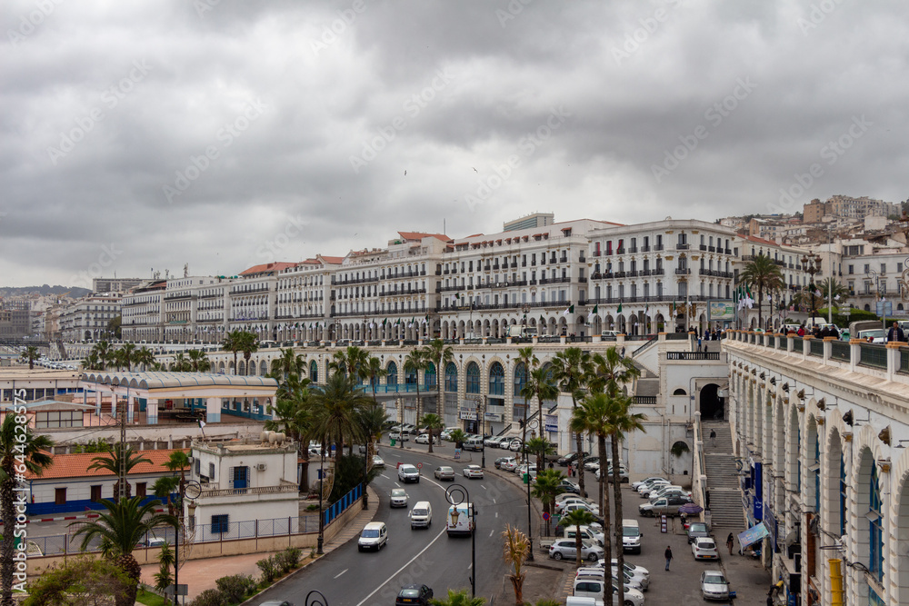 Alger, Algiers, Algeria, 04 19 2023 : panoramic view the Boulevard Amara Mohamed Rachid. Green palm trees, cars, French colonial Renaissance buildings. Cloudy sky.