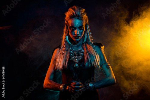 Portrait of fearless savage viking girl make up jewelry yellow blue lights foggy mist isolated on black background