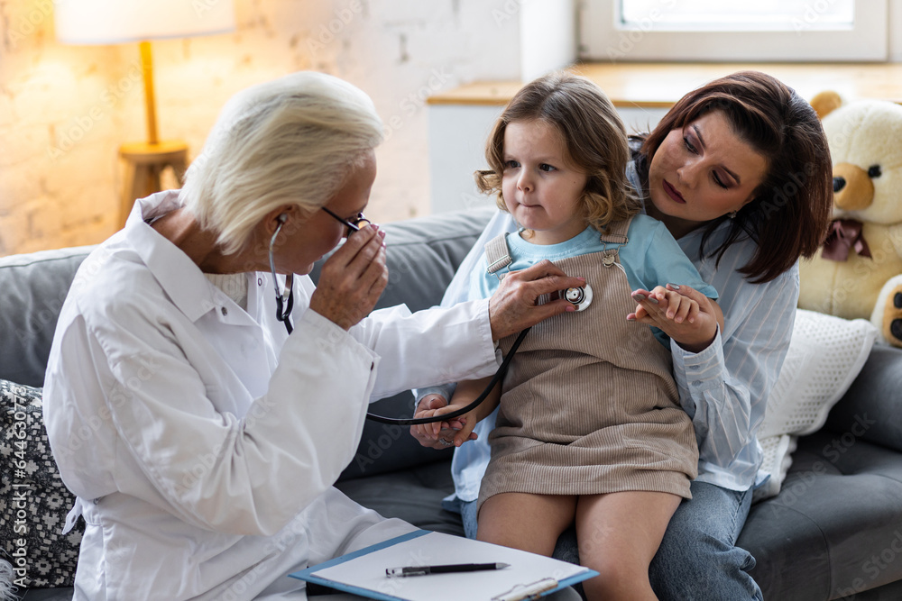 Obraz premium Concept healthcare medical assistance, insurance. Kind senior female paediatrician doctor examining little child sitting on mother's laps, during home visit or clinic check up. Prescribing treatment