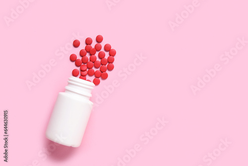 Jar with scattered pills on pink background