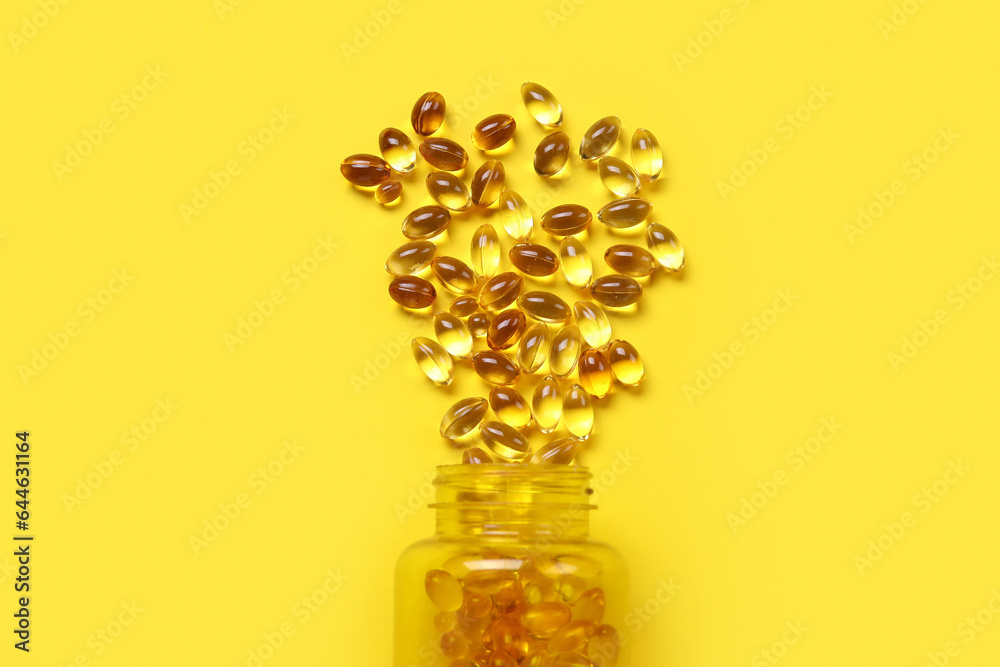 Jar with scattered pills on yellow background