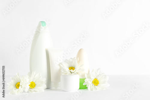 Different cosmetic products and chamomile flowers on white background